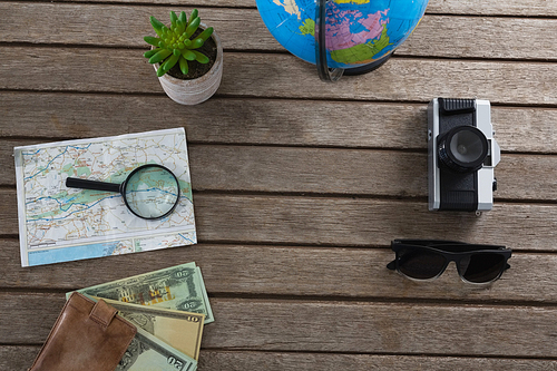 Overhead of currency notes and travelling accessories on wooden plank