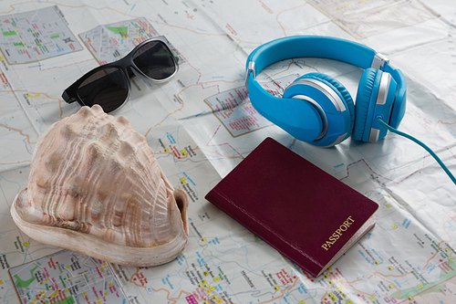 Close-up of sunglasses, headphones, passport and seashell on map