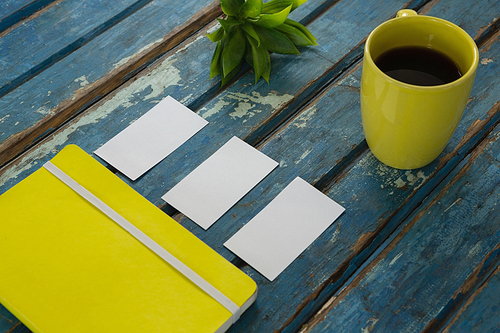 Overhead of blank visiting cards, diary, flora and black coffee on wooden plank