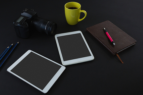 Close-up of digital tablet, black coffee, camera, organizer and pen on black background