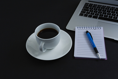 Close-up of black coffee, pen, notepad and laptop on black background