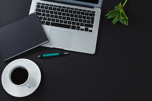 Overhead of black coffee, organizer, pen and laptop on black background