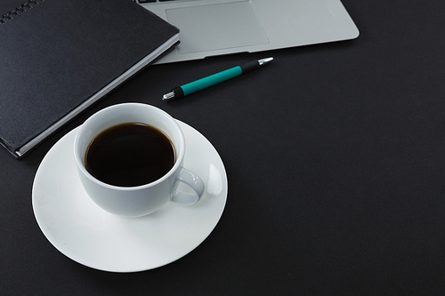 Close-up of pen, organizer, black coffee and laptop on black background