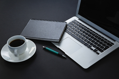 Close-up of pen, organizer, black coffee and laptop on black background