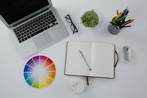 Overhead of laptop, spectacles, color swatch and stationery on white background