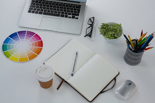 Overhead of laptop, spectacles, color swatch and stationery on white background