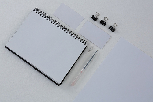 Overhead of book, paper clip, visiting cards and blank paper on white background