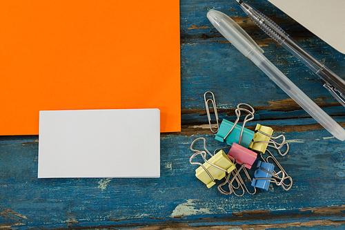 Overhead of book, paper clip, visiting cards and blank paper on wooden plank