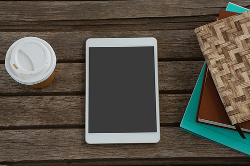 Overhead of disposable glass, books and digital tablet on wooden plank