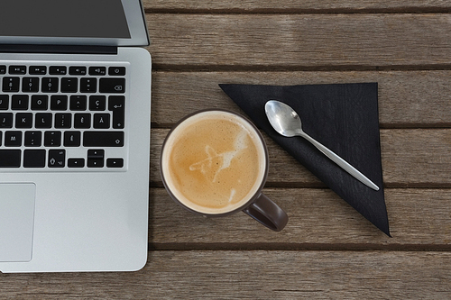 Overhead of laptop, spoon, napkin and coffee on wooden plank