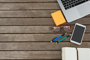 Overhead of mobile phone, laptop, pen, sticky note, spectacles and organizer on wooden plank