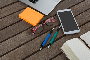 Overhead of mobile phone, laptop, pen, sticky note, spectacles and organizer on wooden plank