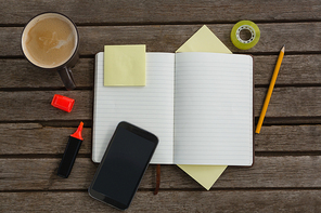 Overhead of organizer, coffee, mobile phone and stationery on wooden plank