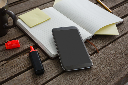 Close-up of organizer, coffee, mobile phone and stationery on wooden plank