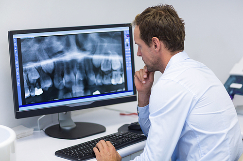 Attentive dentist examining an x-ray on computer in dental clinic