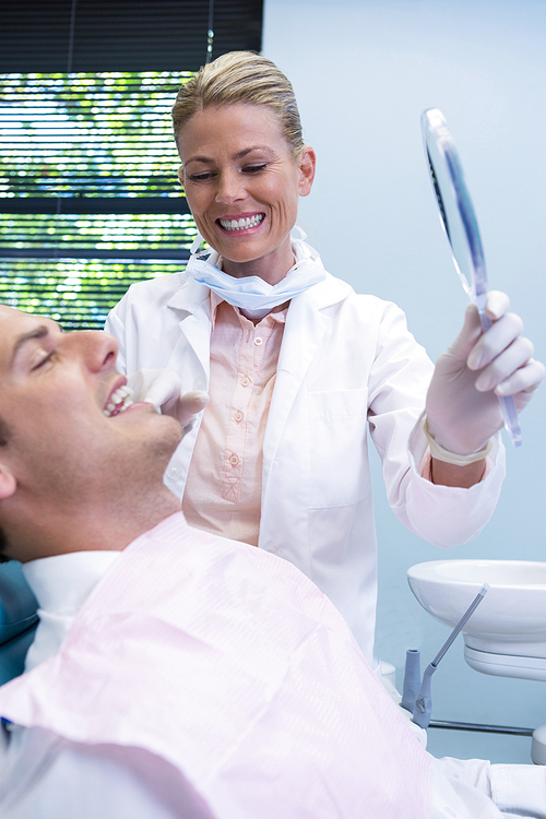 Dentist showing mirrior to patient at dental clinic