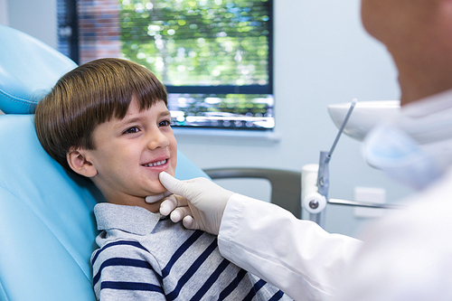 Smiling boy looking at dentist while sitting on chair in medical clinic