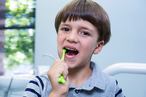 Portrait of boy brushing teeth while sitting on chair at medical clinic