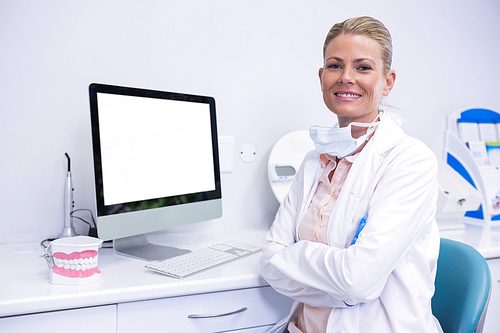 Portrait of smiling dentist working while sitting by computer at medical clinic
