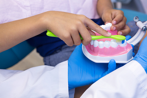Close-up of dentist and boy brushing dentures at clinic