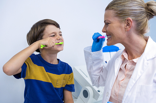 Happy dentist and boy brushing teeth against wall at clinic