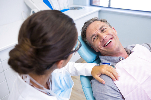Happy patient sitting on chair while looking at dentist in medical clinic