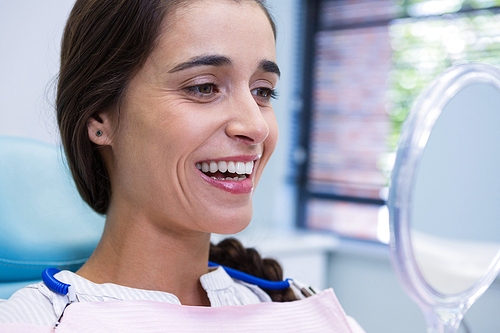 Portrait of patient smiling while looking at mirror in dental clinic
