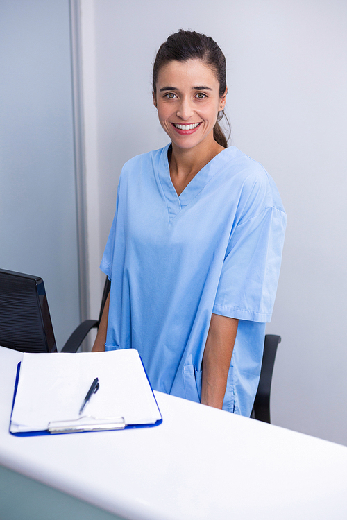 Portrait of smiling doctor standing at desk against wall in dental clinic