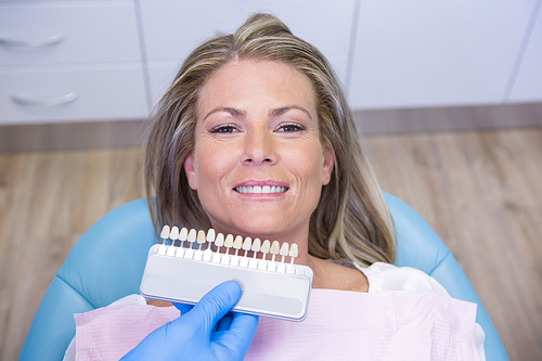 High angle view of dentist holding tooth whitening equipment by smiling patient at clinic
