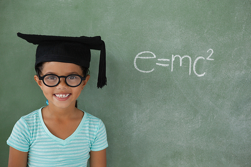 Portrait of young girl with graduation hat against chalk board