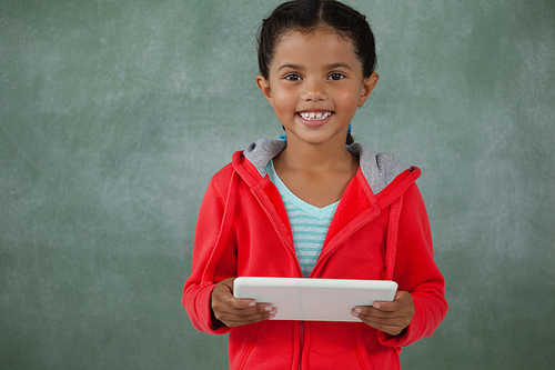 Young girl holding digital tablet against chalk board