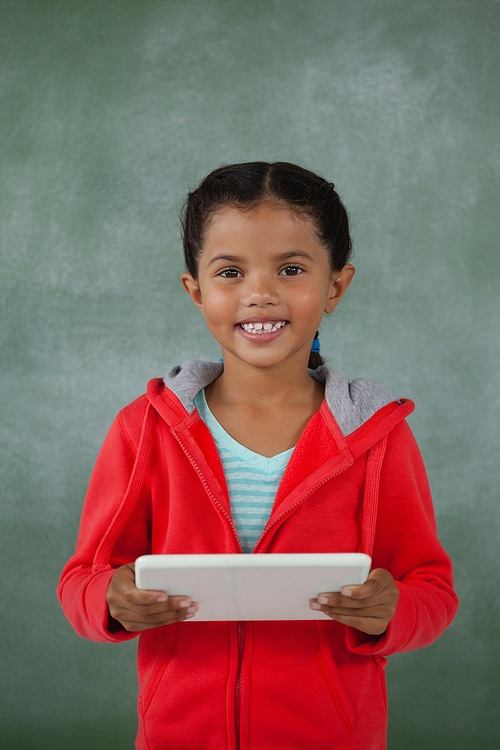 Young girl holding digital tablet against chalk board