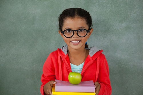 Portrait of young girl in glasses holding apple and books