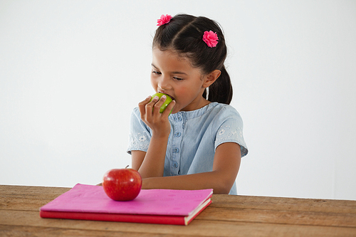 Adorable schoolgirl eating apple against white background