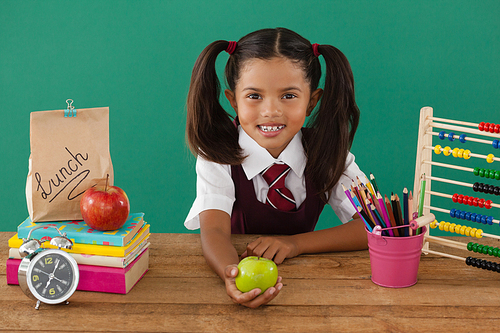 Adorable schoolgirl holding a green apple against green background