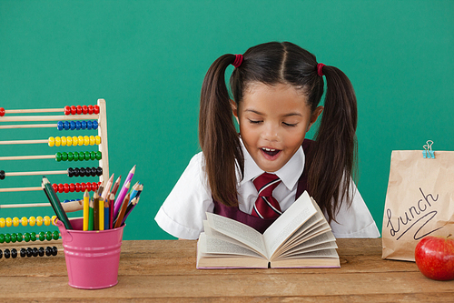 Adorable schoolgirl reading a book against green background