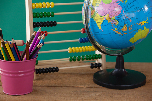 Close-up of globe, penholder and abacus on wooden table