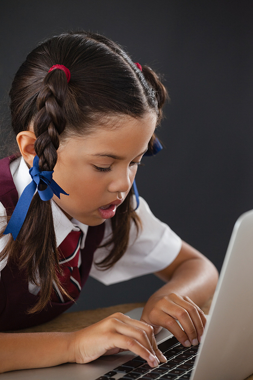 Schoolgirl using laptop against blackboard in classroom