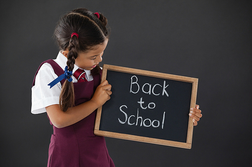 Schoolgirl holding slate with text against blackboard in classroom