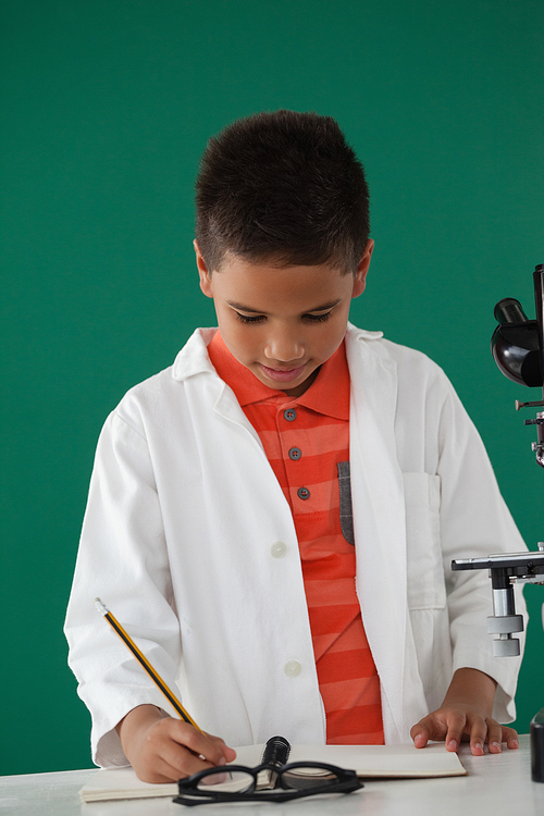 Schoolboy writing on book against green background