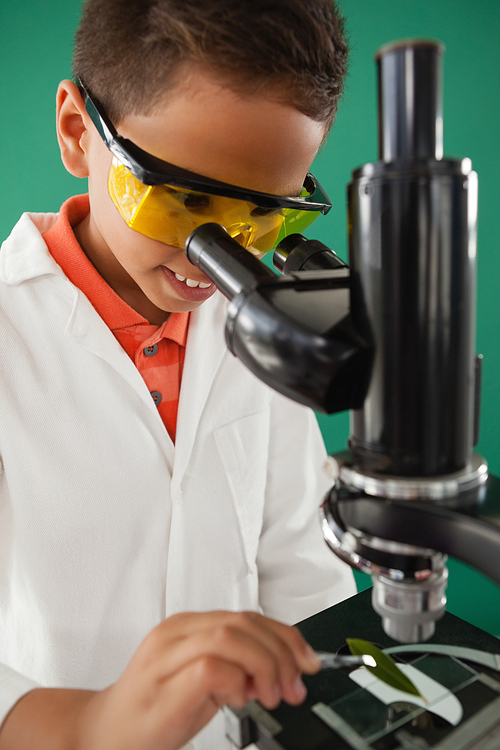 Schoolboy using microscope against green background