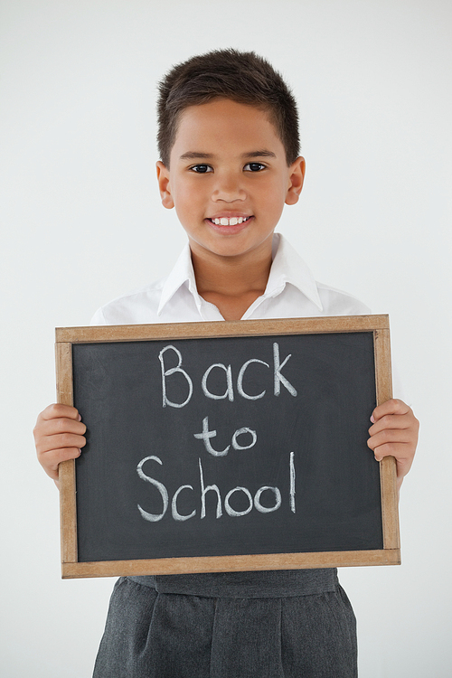 Portrait of schoolboy holding writing slate with text back to school against white background