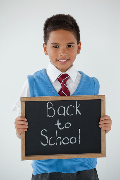 Portrait of schoolboy holding writing slate with text back to school against white background