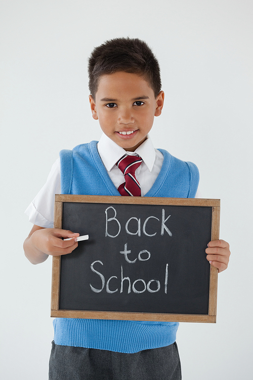 Portrait of schoolboy holding writing slate with text back to school against white background