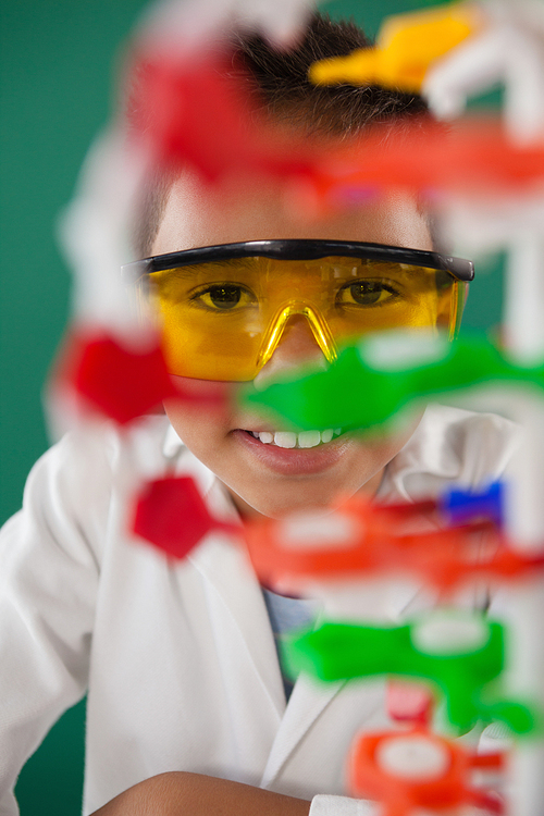 Portrait of smiling schoolboy experimenting molecule model in laboratory at school