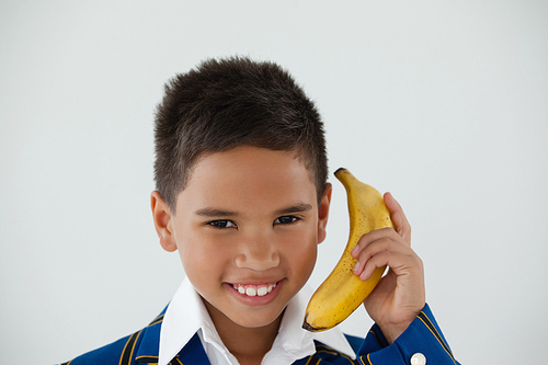 Portrait of schoolboy holding banana against white background