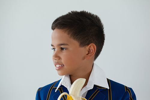 Thoughtful schoolboy having banana against white background