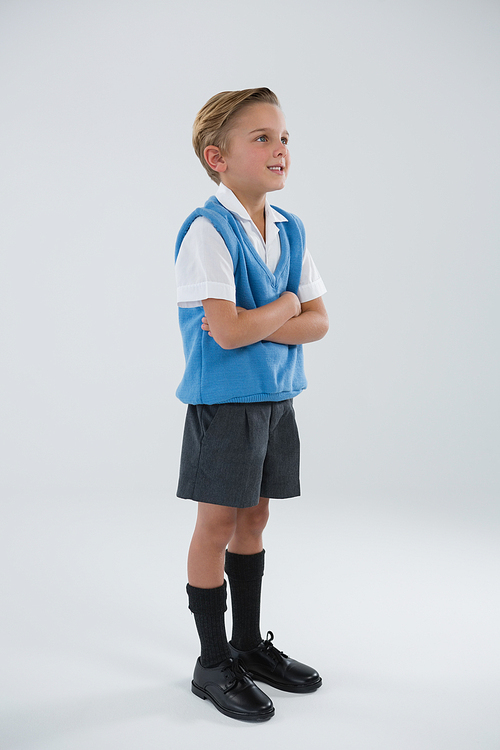 Smiling schoolboy standing with arms crossed against white background