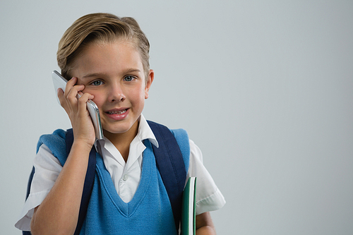 Portrait of happy schoolboy talking on mobile phone against white background