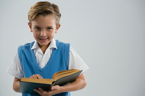 Portrait of schoolboy reading book against white background